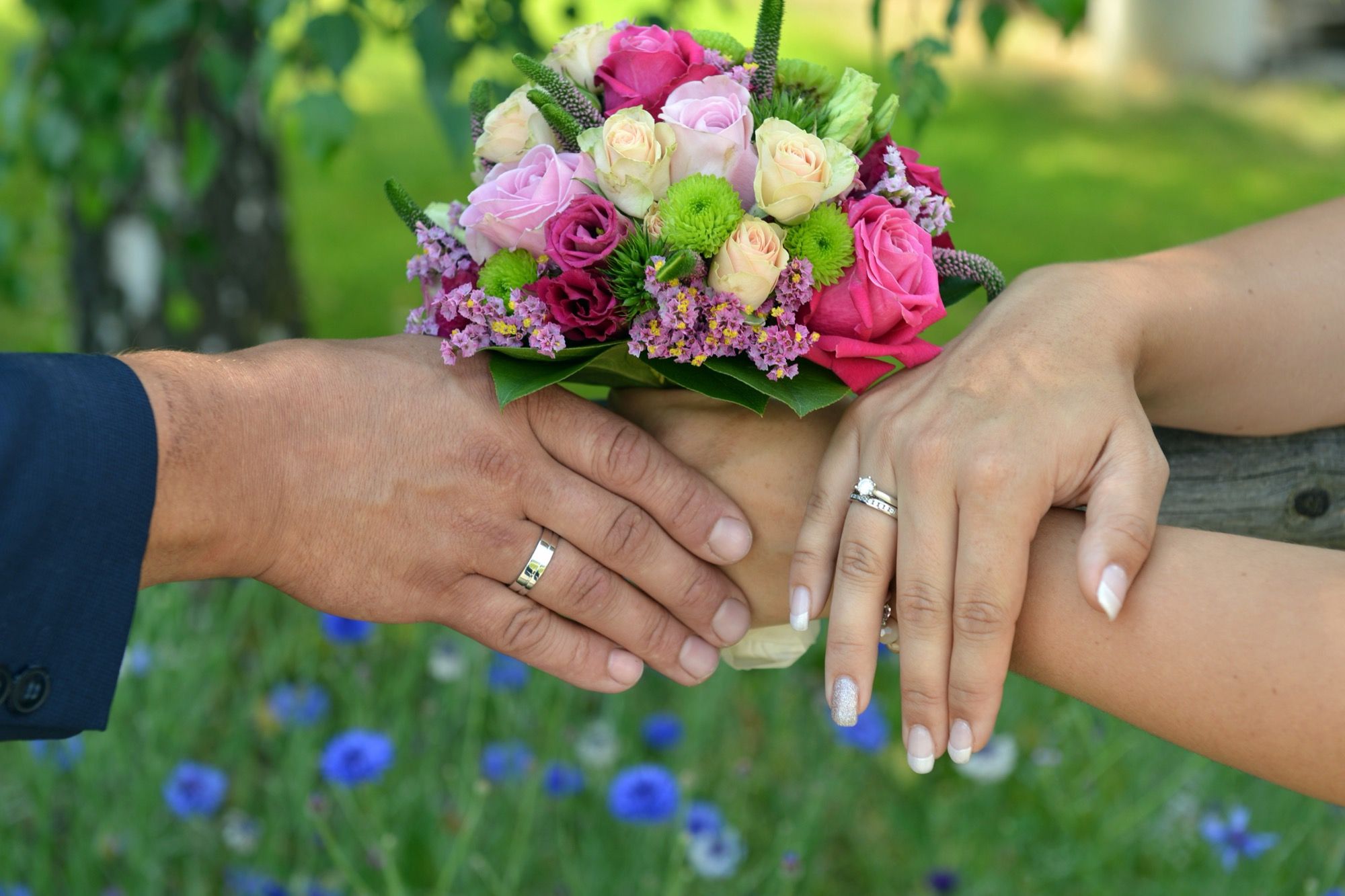 Le mani degli sposi con le fedi e il bouquet
